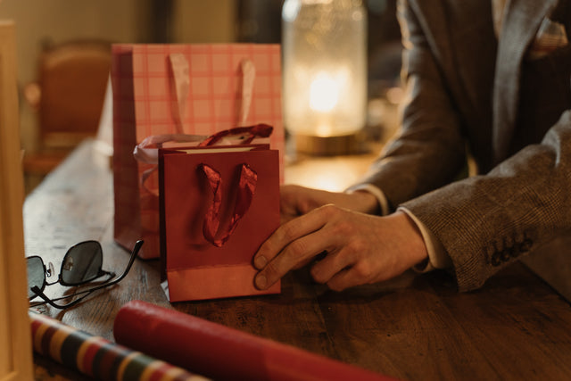 Picture of red gift bags and wrapping paper on a wooden table, a man's hand arranging them